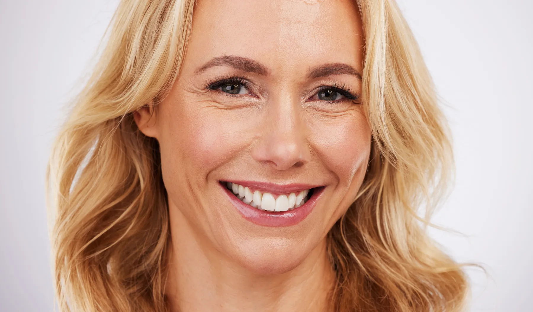 A blonde woman smiling with a white background