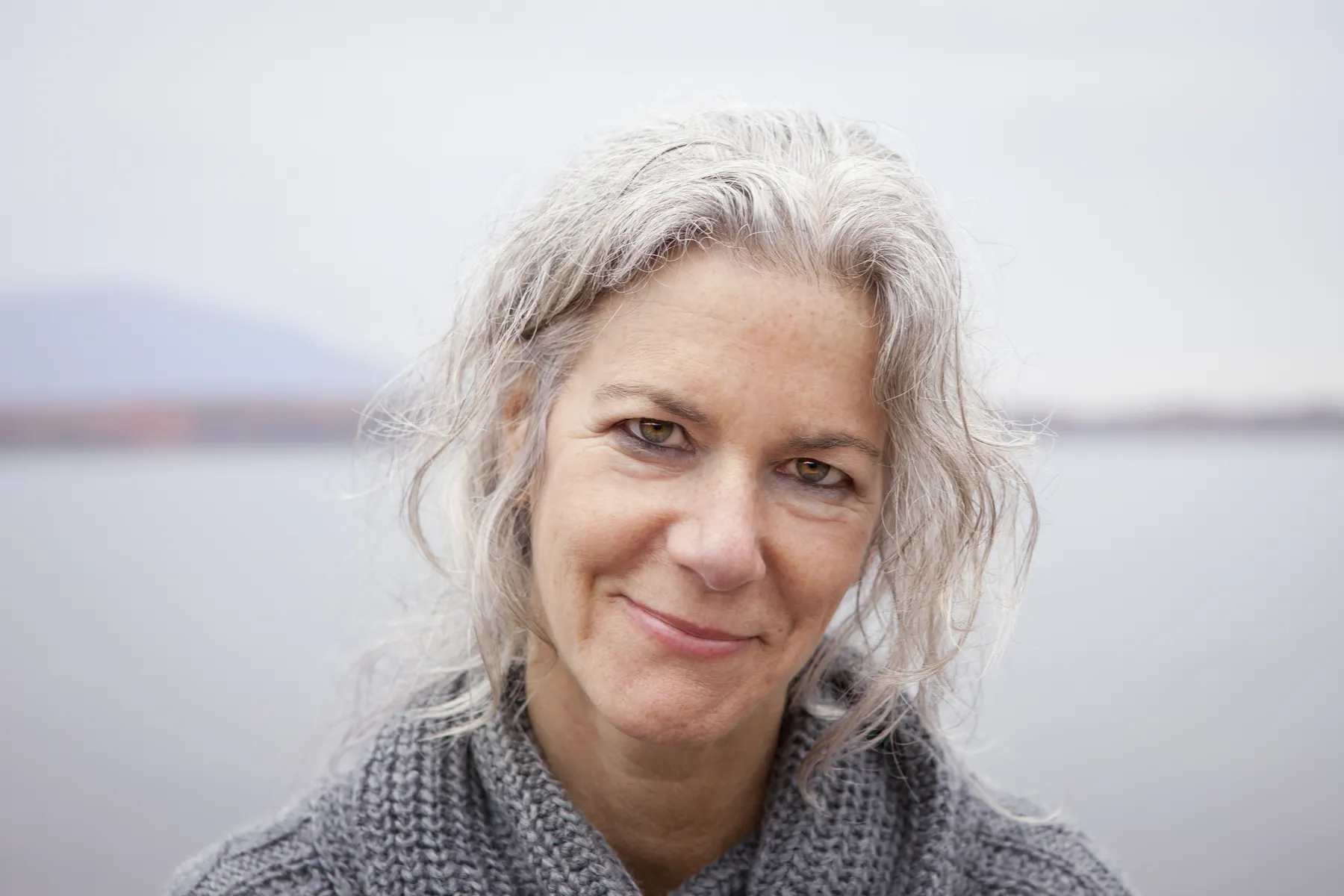 A calm woman with gray hair smiling outdoors