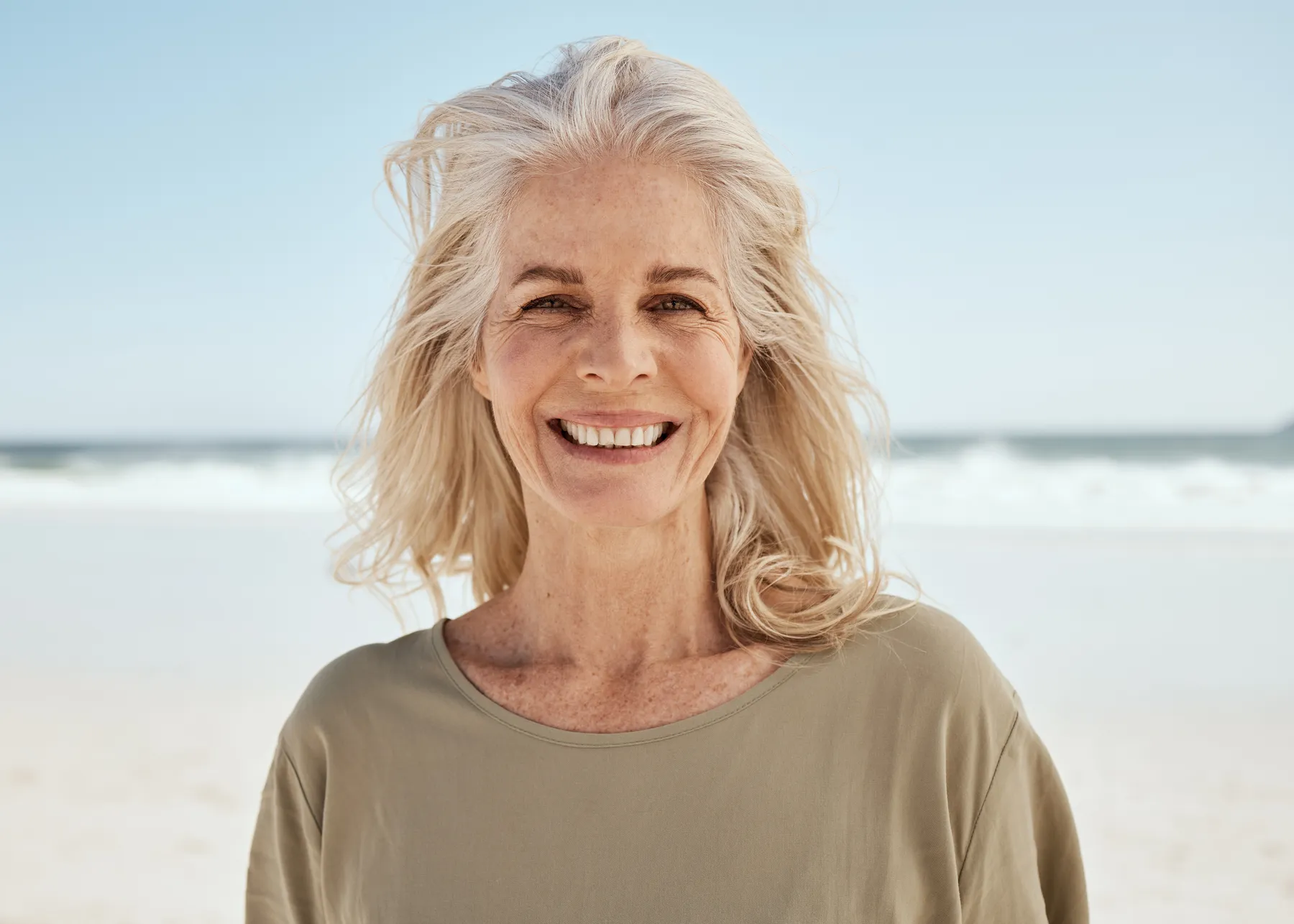 A senior woman smiling on a bright beach day