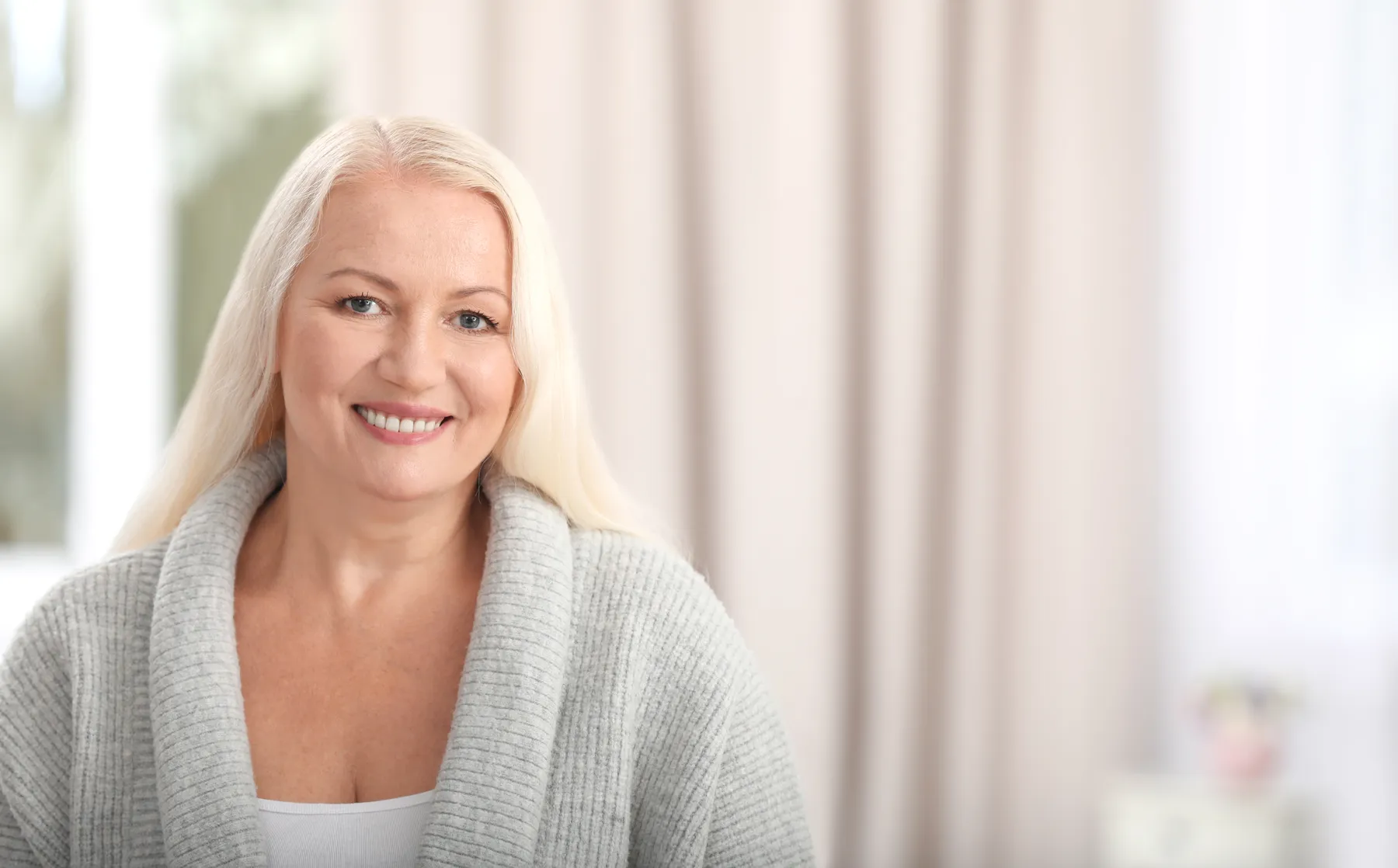 A smiling woman in a gray cardigan indoors