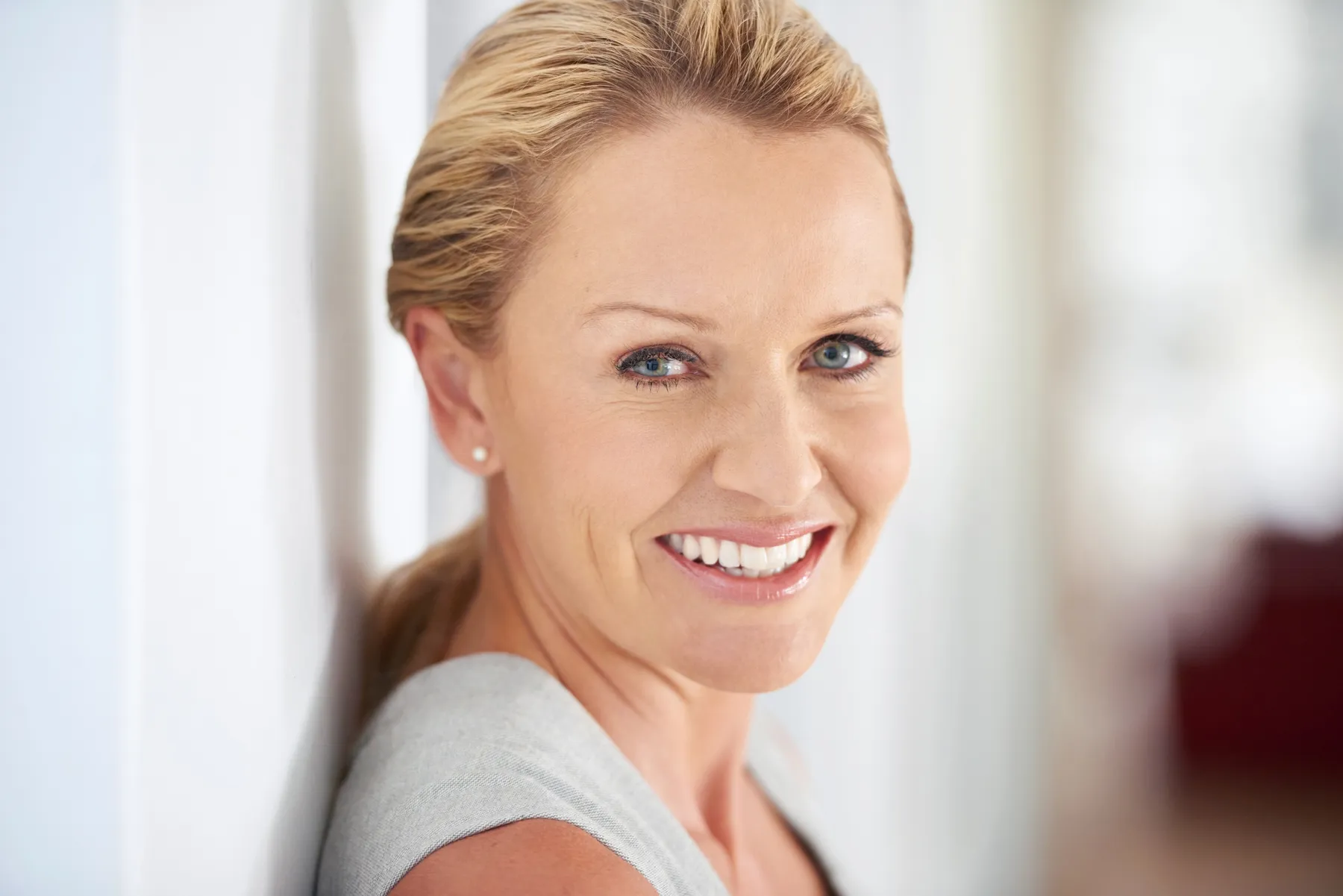 A smiling woman leaning against white wall indoors
