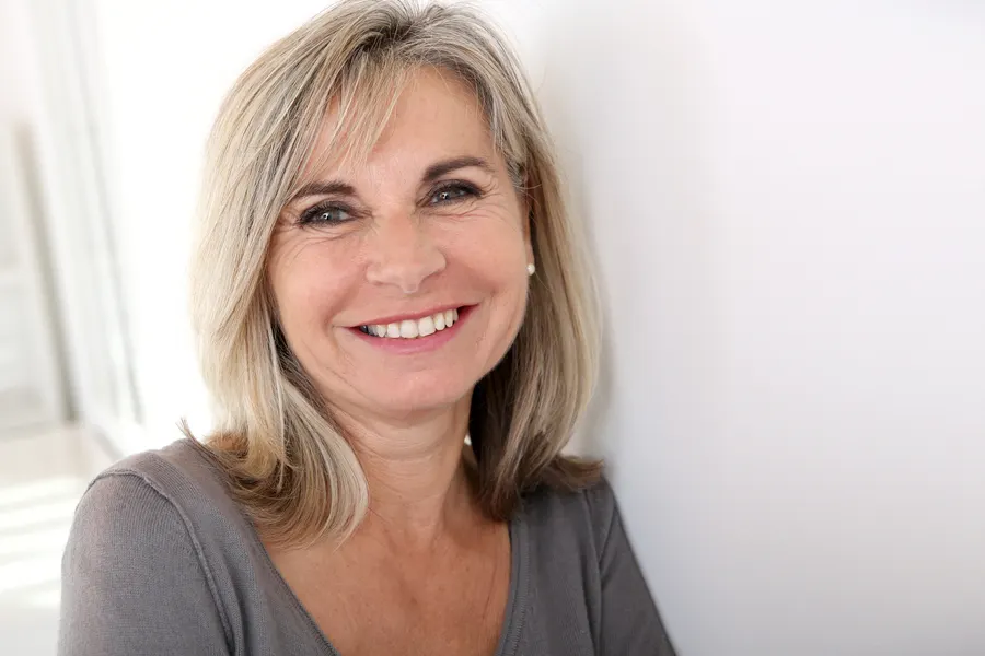 A smiling woman with blonde hair leaning on wall