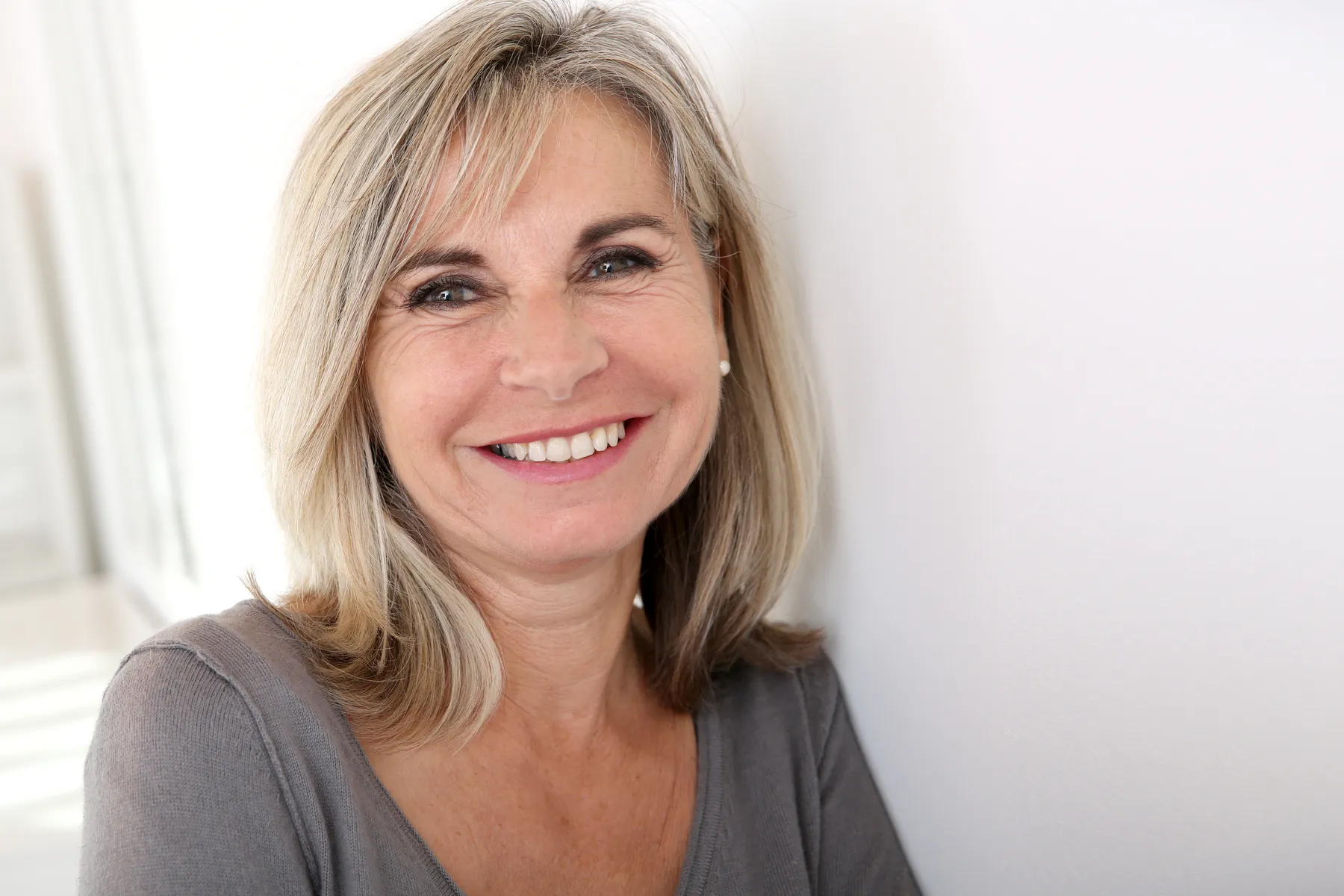 A smiling woman with blonde hair leaning on wall