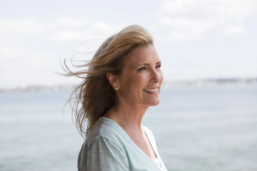 A smiling woman with windblown hair near the water