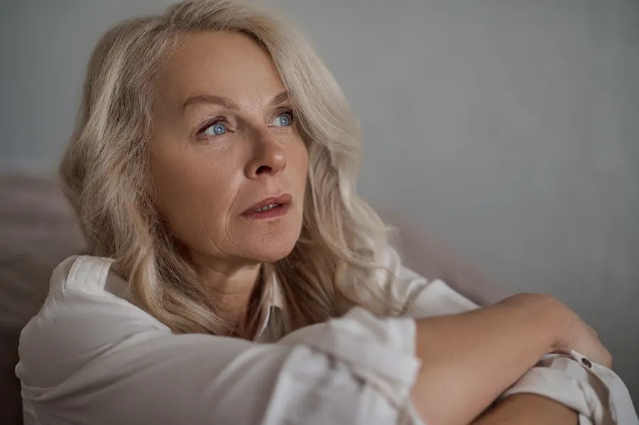 A thoughtful woman with wavy white hair looking up