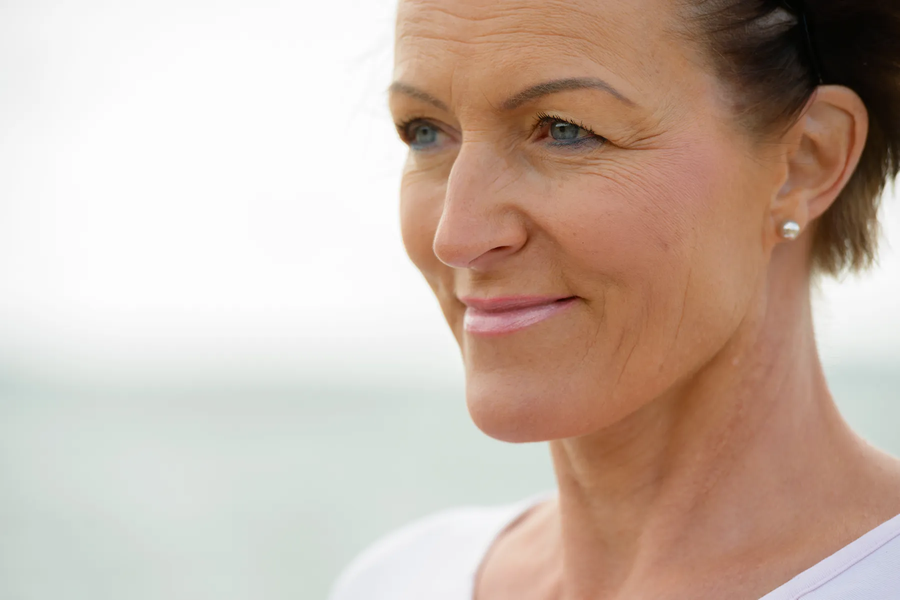 A woman smiles outdoors near a beach