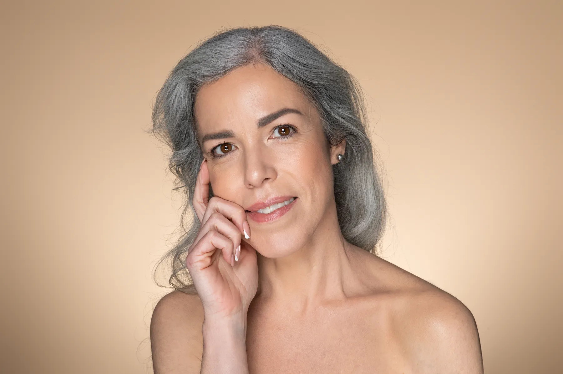A woman with grey hair posing against beige